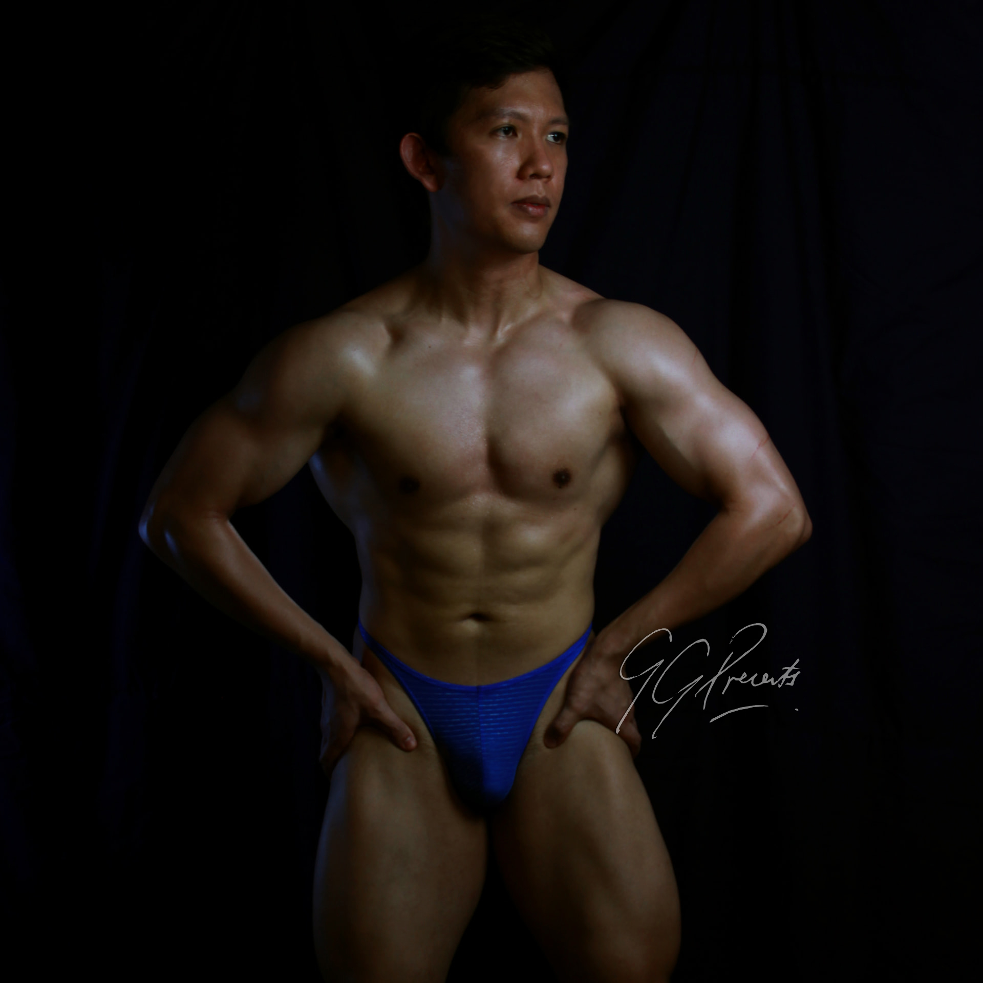 Athlete in cobalt blue posing trunks with hands on hips in low-key studio light